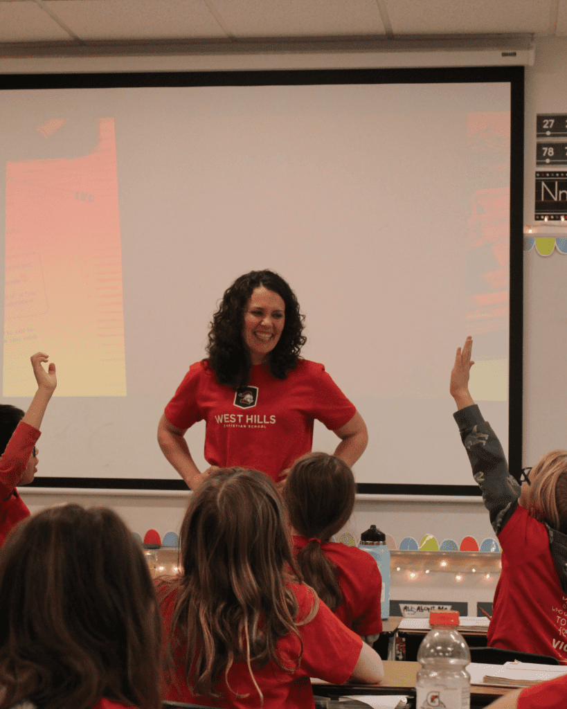 A teacher at West Hills grins ear to ear as numerous students raise their hands in class.